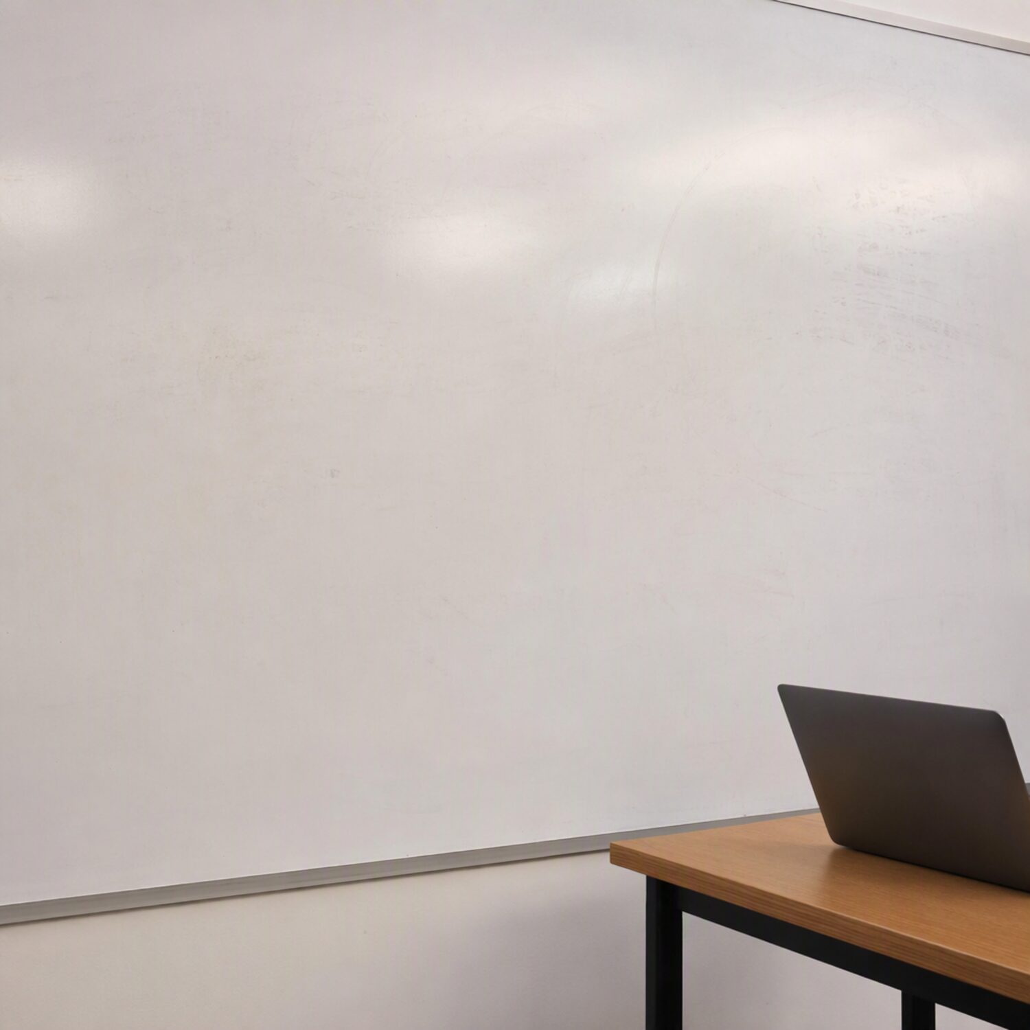 A whiteboard wall beside a table with a laptop