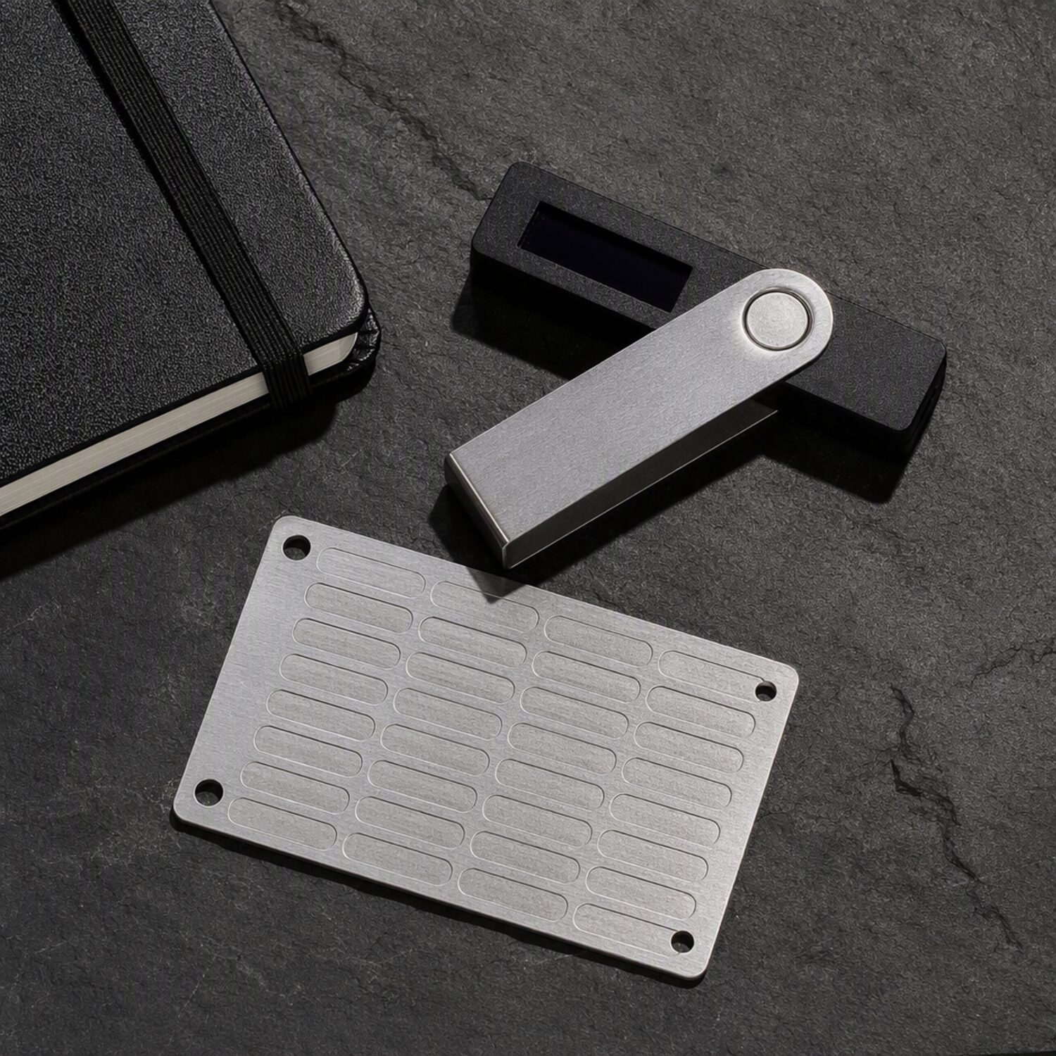 A hardware wallet and steel backup plate on a slate surface