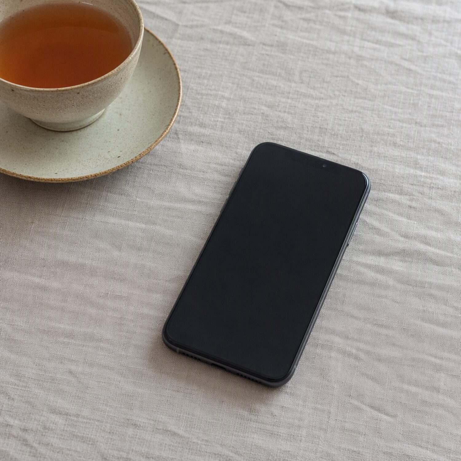 A phone face up beside a cup of tea