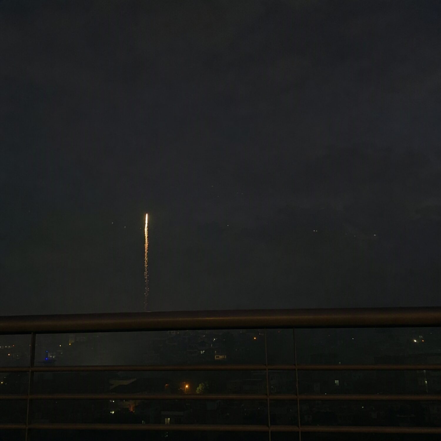 A single firework trail over a rooftop railing