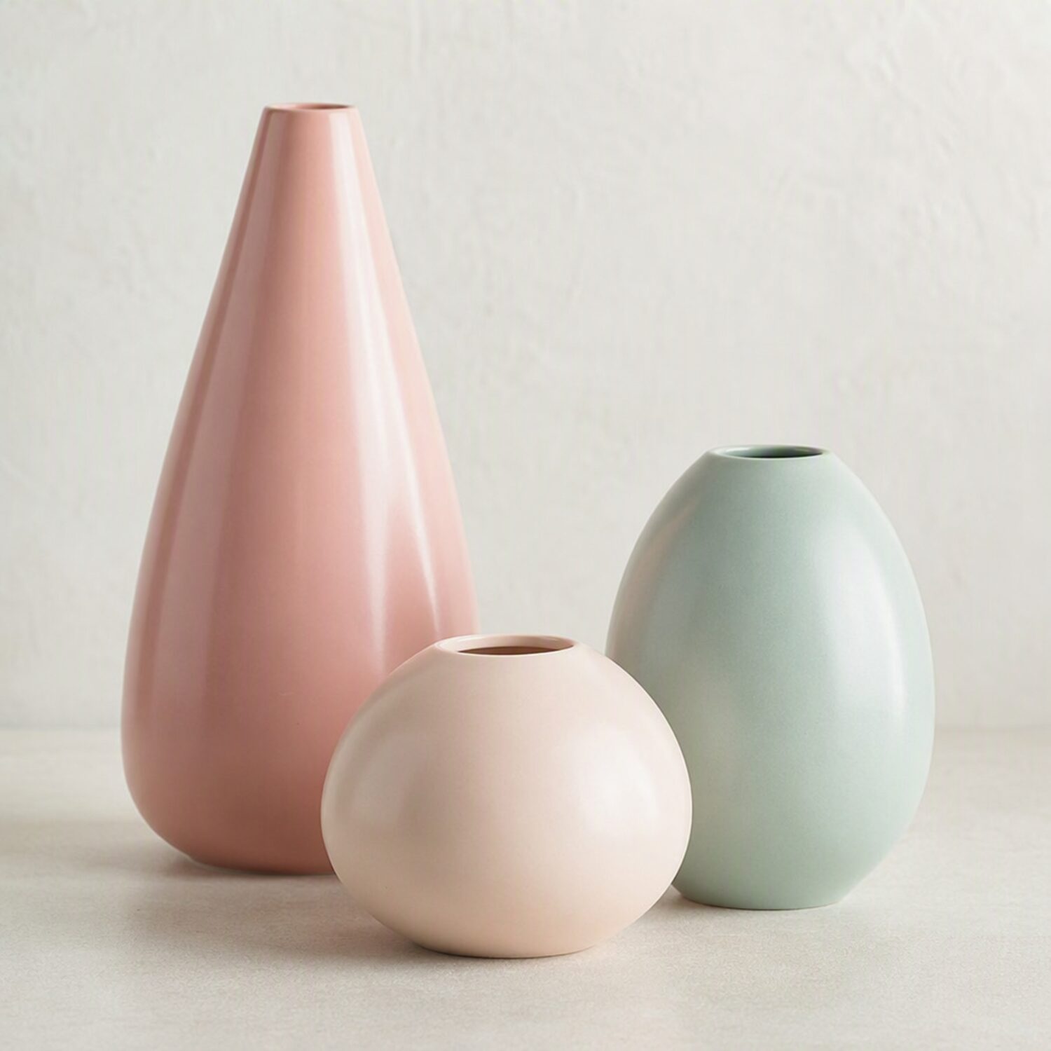 Three pastel ceramic shapes casting soft shadows